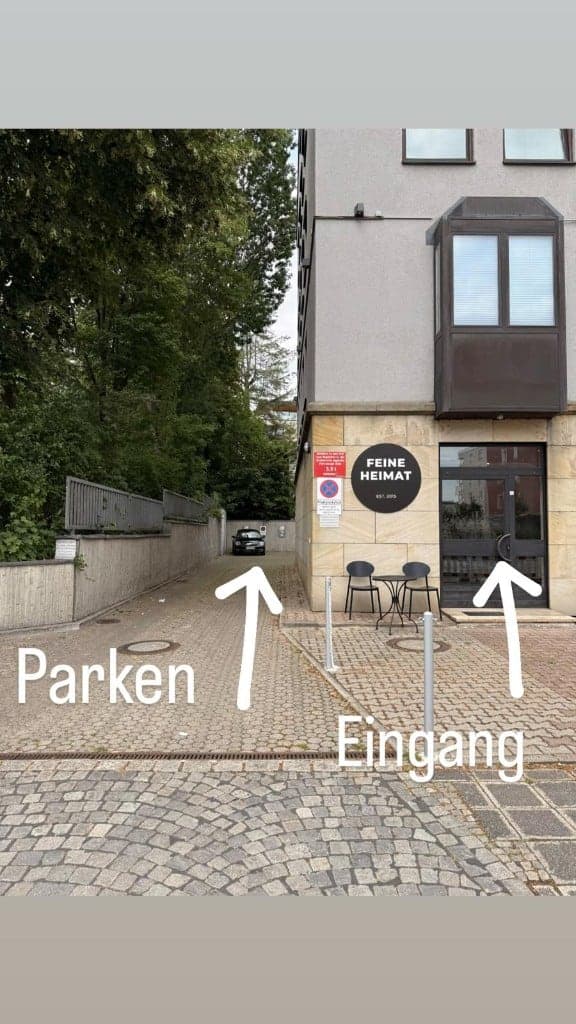 Einfahrt zum Parkplatz und Eingang des Feine Heimat Stores mit Wegweisern